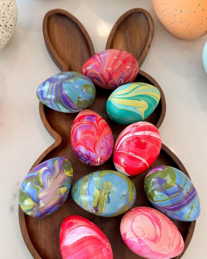 Colorful marbled Easter eggs arranged on a wooden bunny-shaped tray from @kelsimsavage showing vibrant swirling paint patterns for easter egg decorating ideas for adults