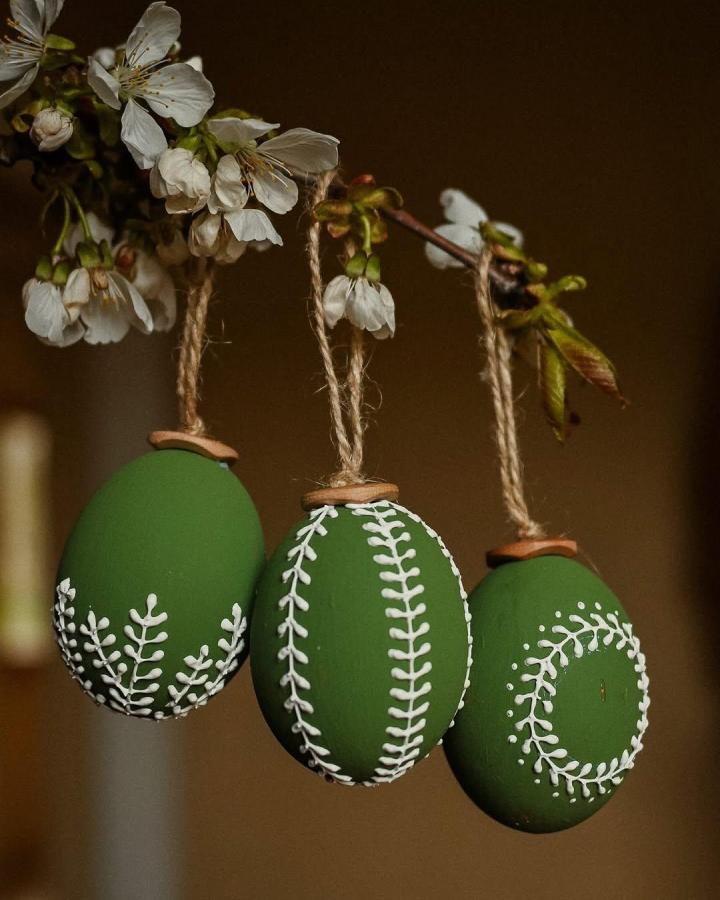 Green matte botanical Easter eggs hanging from branches from @tvorit_a_lubit showcasing delicate white leaf patterns for easter egg decorating ideas for adults