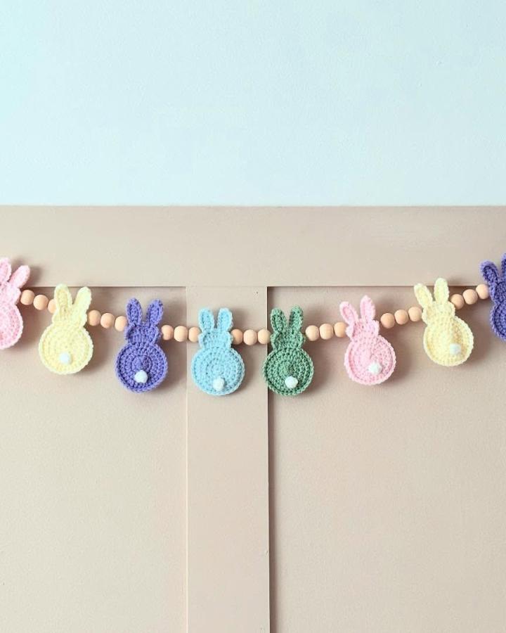 crocheted pastel bunny garland with wooden beads Easter garland ideas from @craftymummyof3 hanging on beige wall panel