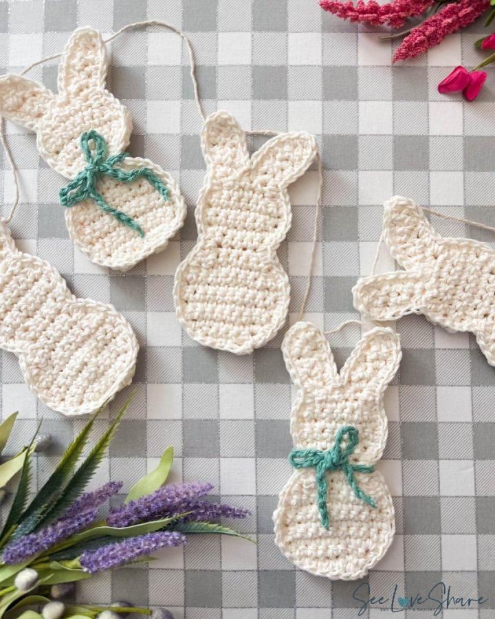 Creamy crochet bunny garland with teal bows by @yarnspirations easter garland ideas on checkered cloth with floral accents.