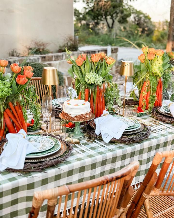 Bright carrot vases with tulips and greenery on a gingham tablecloth from @thevelvettable perfect easter place setting ideas.