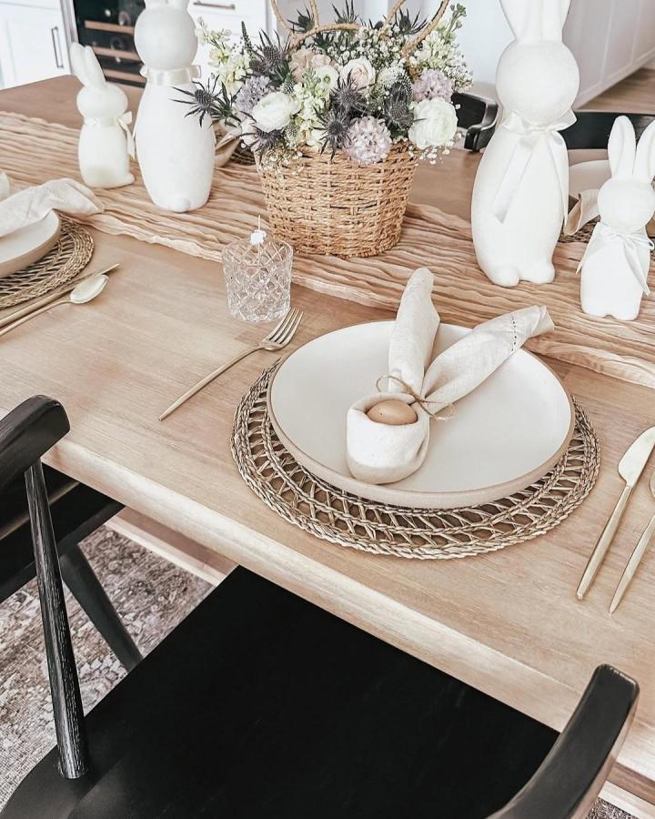 Creamy white ceramic bunnies and natural woven placemats on a wooden table from @jensgathernest for Easter place setting ideas.