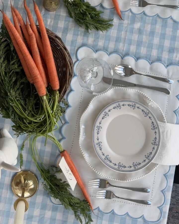 Orange carrots tied with place cards on blue and white gingham tablecloth from @tableshoppeco. Rustic elegant easter place setting ideas.