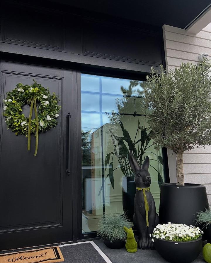 Black door Easter porch decor ideas from @home_by_joann featuring a green wreath, black planters, and a decorative bunny statue.
