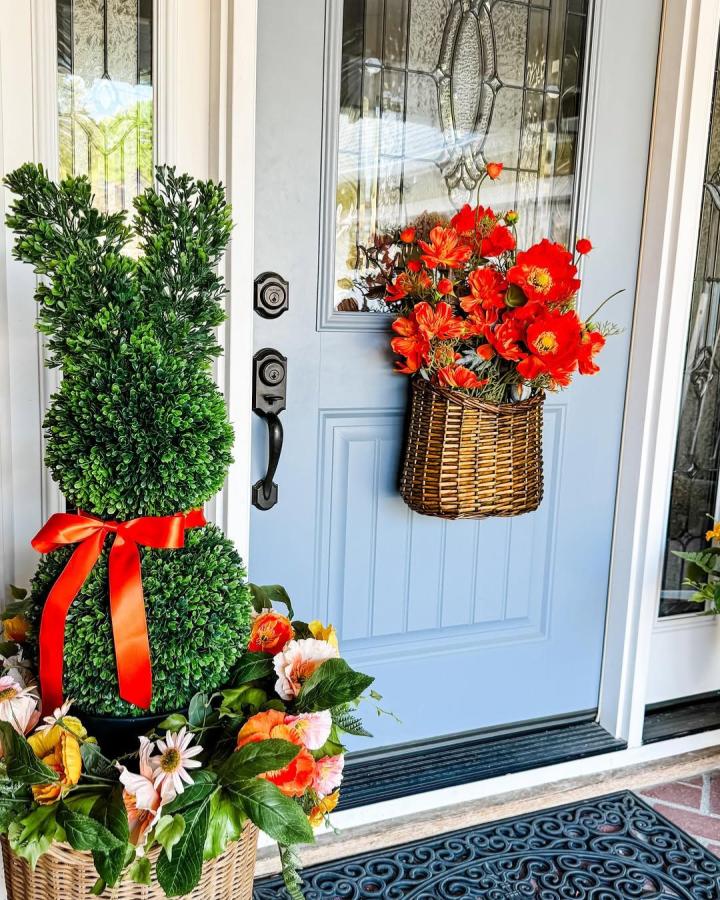 Green boxwood bunny topiary and vibrant orange floral basket on a baby blue door from @jeannaloveschristmas for easter porch decor ideas.