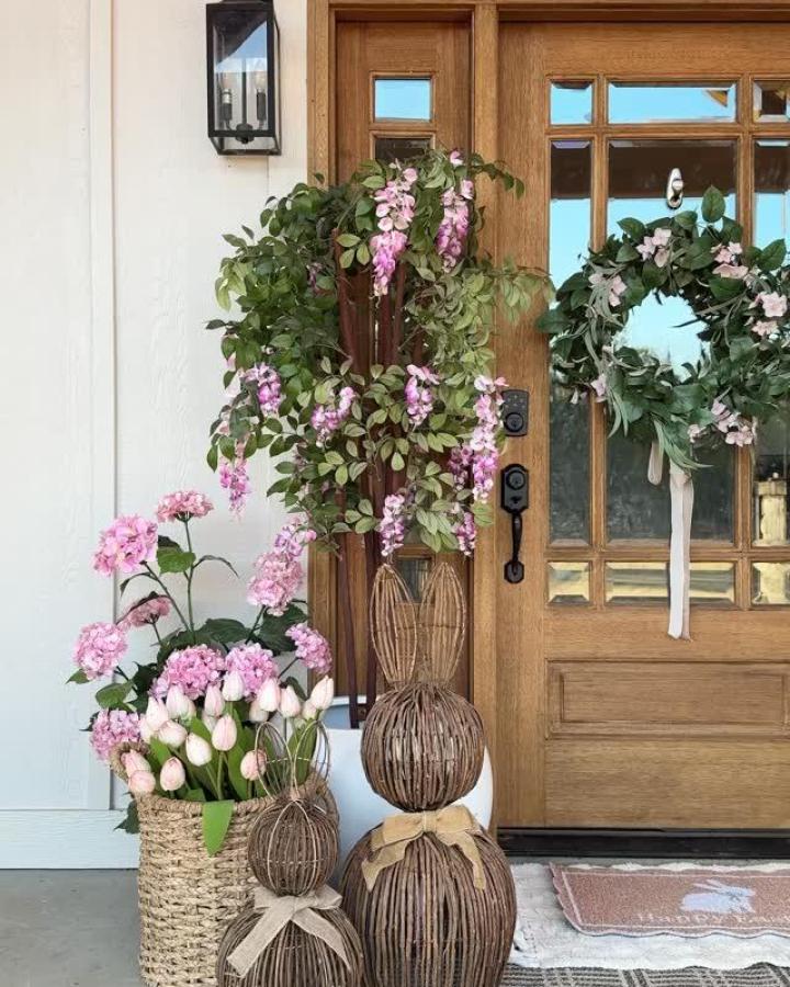 Natural wicker bunny statues with pink flowers and wooden door from @ourwintonhome Easter porch decor ideas.
