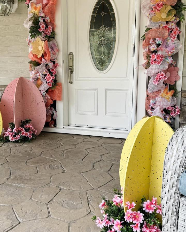 Pink and yellow oversized Easter eggs with pink flower accents on a porch from @jeannaloveschristmas playful easter porch decor ideas