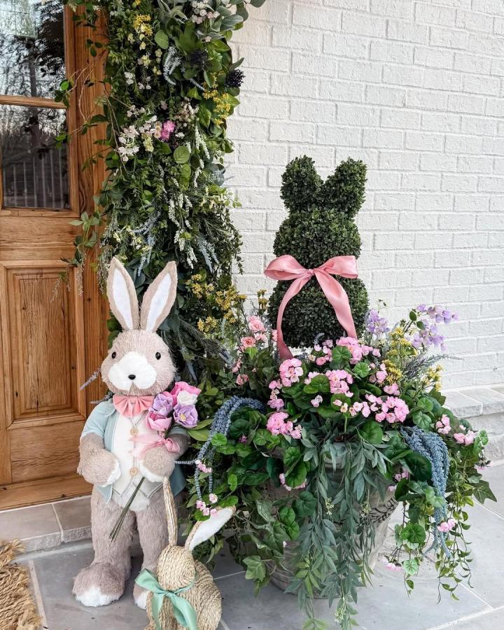 Green bunny topiary with pink ribbon, pastel flower planter, and fabric Easter bunny on porch by @ashleymariesavage. Easter porch decor ideas.