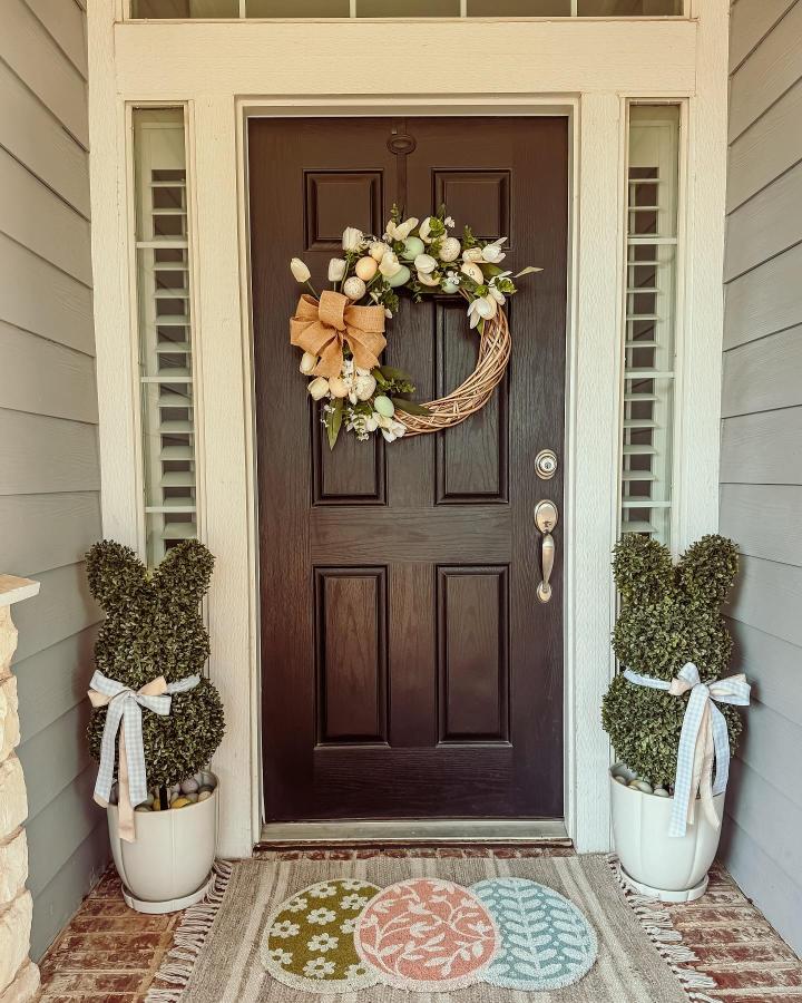 green bunny topiaries and pastel egg rug on front porch from @courtneyfitzp01 with burlap bows and spring wreath for easter porch decor ideas