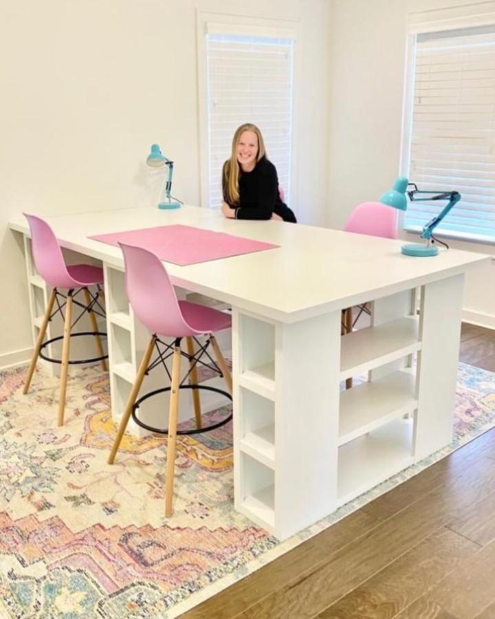White craft table with ikea kallax craft room ideas showing built-in shelves and pastel pink chairs under natural light
