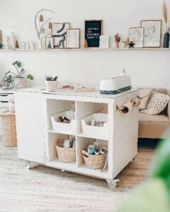 White wooden rolling storage island with cubbies and baskets from @idoitmyself.be. Ikea kallax craft room ideas with added roll holder and wheels.