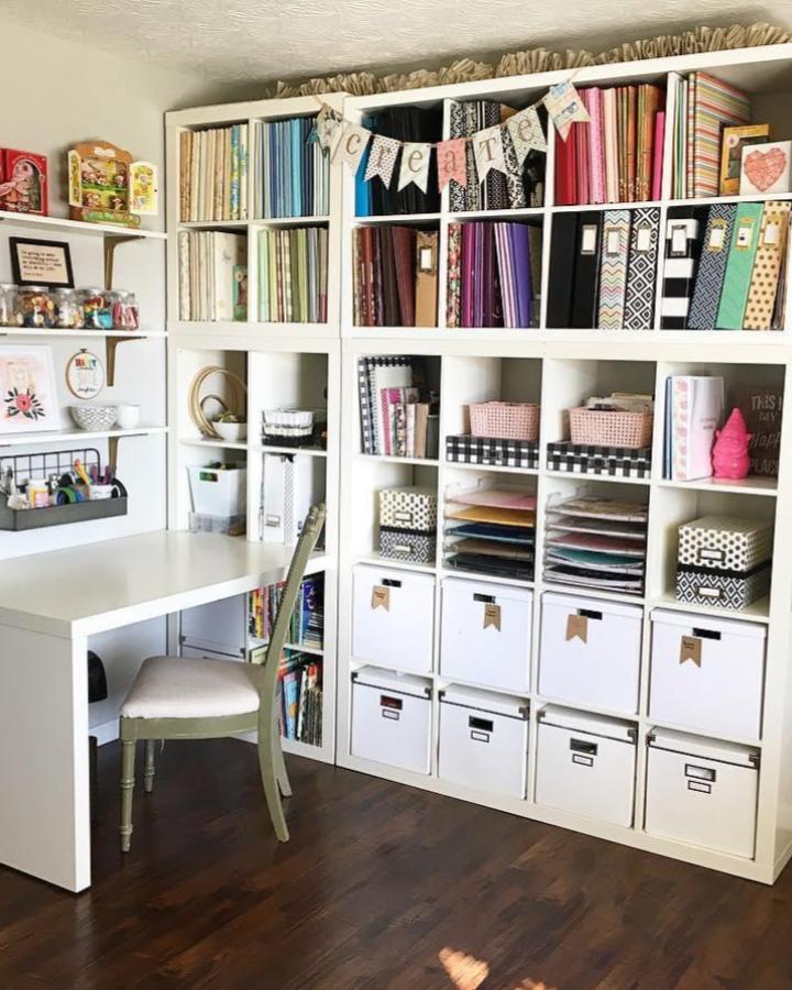 White Ikea Kallax craft room shelves with colorful paper and labeled storage bins from @bookgirlcreations. Organized and inviting craft space.