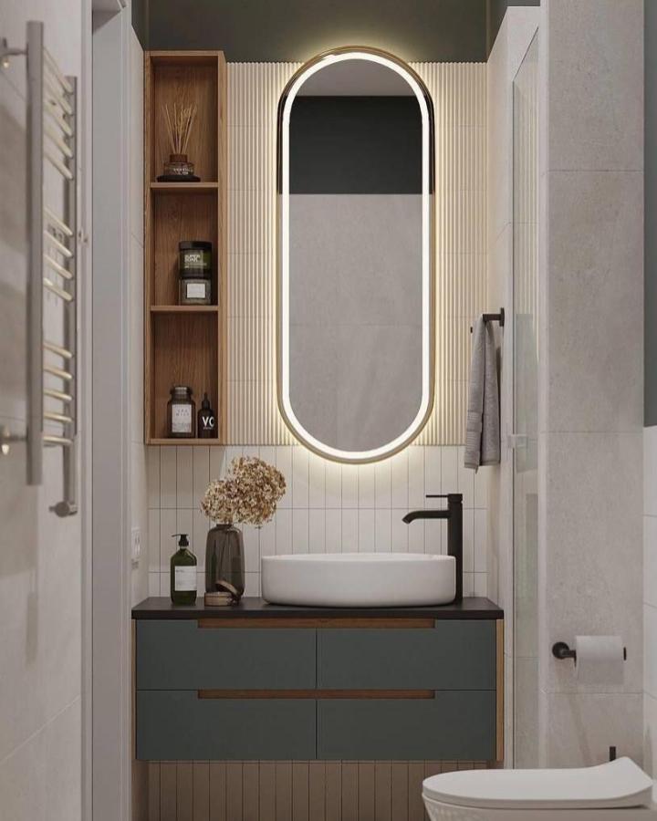 Backlit oval mirror with LED light in small bathroom by @aesthetichime.mnl featuring wood shelves and black fixtures perfect for bathroom mirror ideas for small spaces