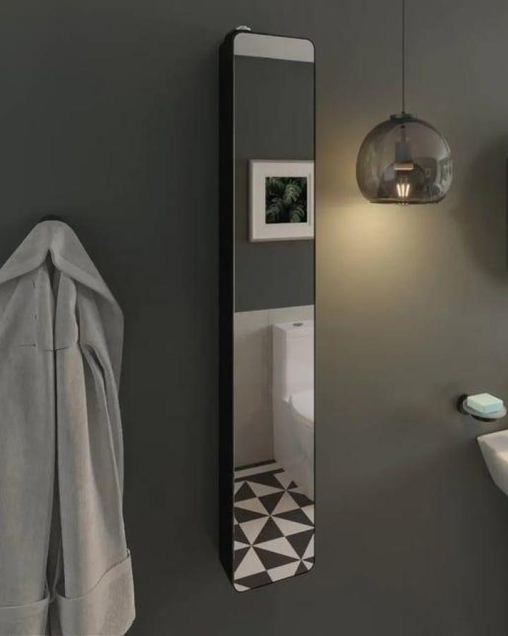 Slim tall pivoting mirror cabinet with matt black frame from Plumbworld hanging on dark wall in a small bathroom reflecting geometric tile floor and framed art.