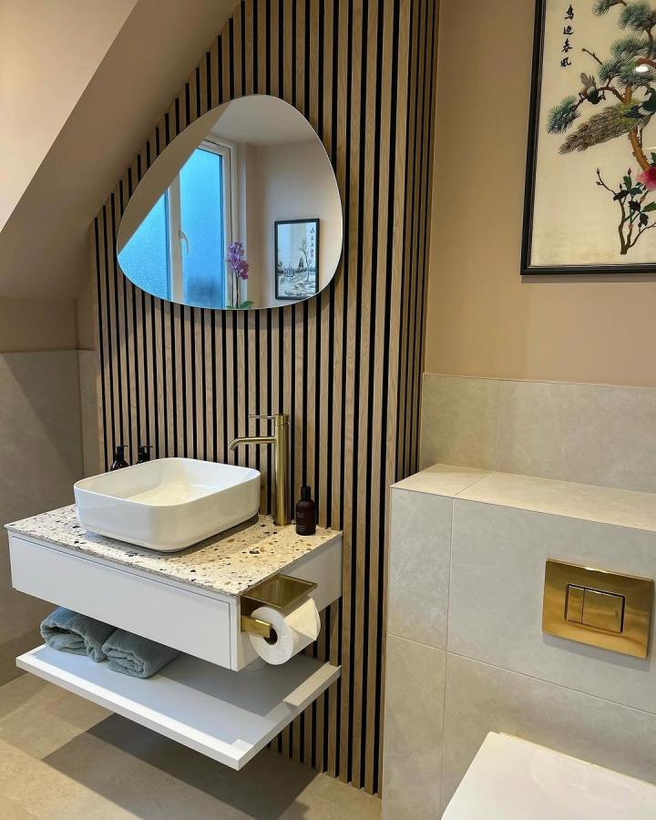 Light wood vertical slat panels in bathroom vanity area from @thegrafterswife. Modern, textured bathroom wall panel ideas with terrazzo countertop and brass fixtures.