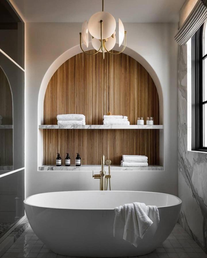 Warm wooden vertical slat bathroom wall panel ideas with marble shelves and gold fixtures from @shadedeggesphotography in modern bathroom setting.