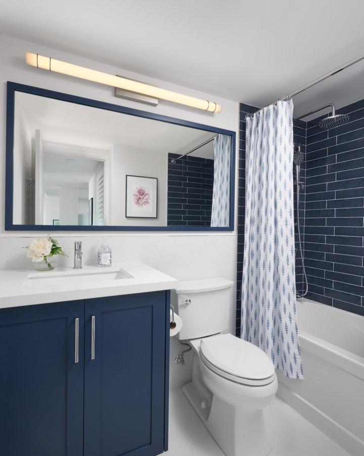 Blue framed mirror and navy vanity in bathroom by @juliabewcyk featuring deep blue tiles and patterned shower curtain blue bathroom decor ideas.