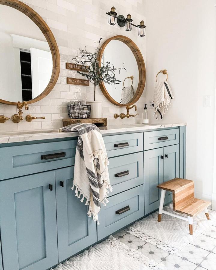 Blue shaker cabinets and wood-framed mirrors in a bathroom from @theryanhaus_ showcase cozy blue bathroom decor ideas with brass fixtures and white tiles.