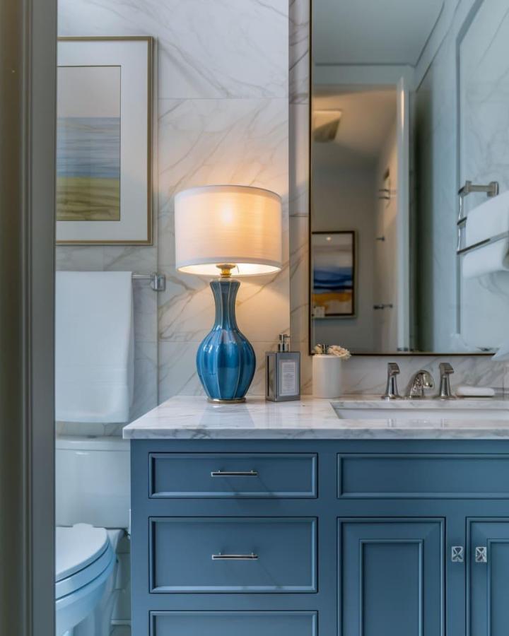 Blue custom cabinetry and ceramic lampshade in a bathroom from Fancy House Design with marble countertops and modern fixtures.
