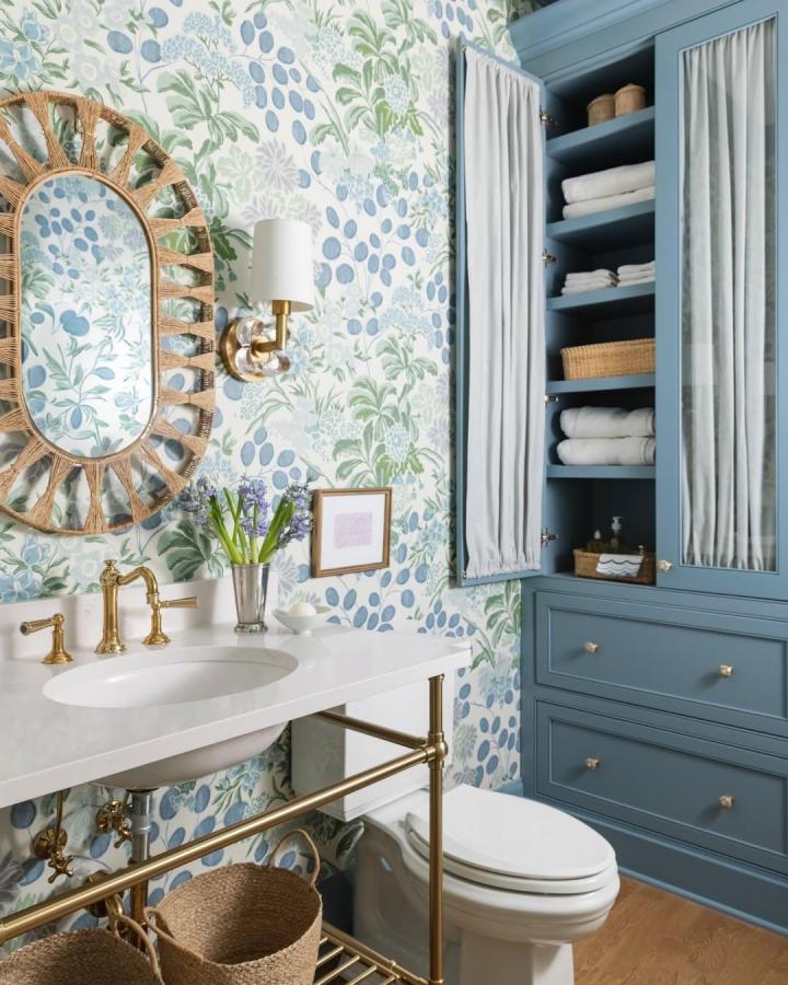 Blue built-in cabinetry and nature-themed wallpaper in a bathroom by @elizabethburchinteriors showing blue bathroom decor ideas with brass accents and woven baskets.