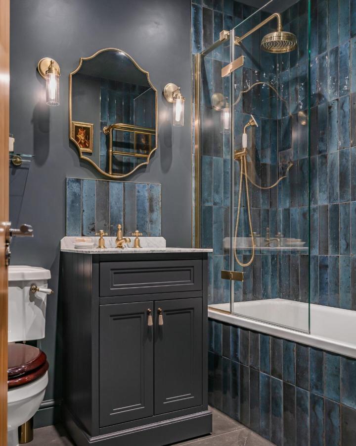 Inky blue tiles and soft blue walls with brass fixtures in a bathroom by @bathroomsbydesignuk showing elegant blue bathroom decor ideas.