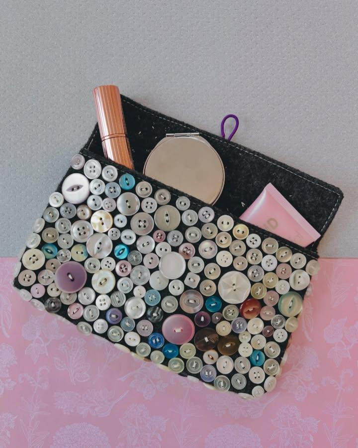 Grey felt makeup bag adorned with assorted buttons from @sumoftheirstories. Charming, textured button crafts for adults project.