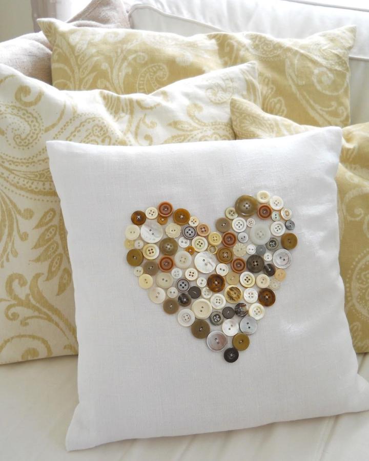Cream and brown button heart pillow on white fabric from ahomemadeliving. Cozy vintage button crafts for adults project.