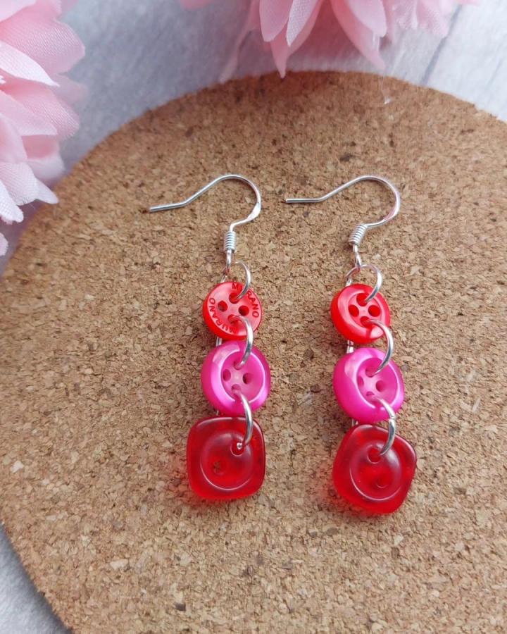 Red and pink button earrings made with linked button crafts for adults by @juniperjanecraft on cork background. Bright and charming.