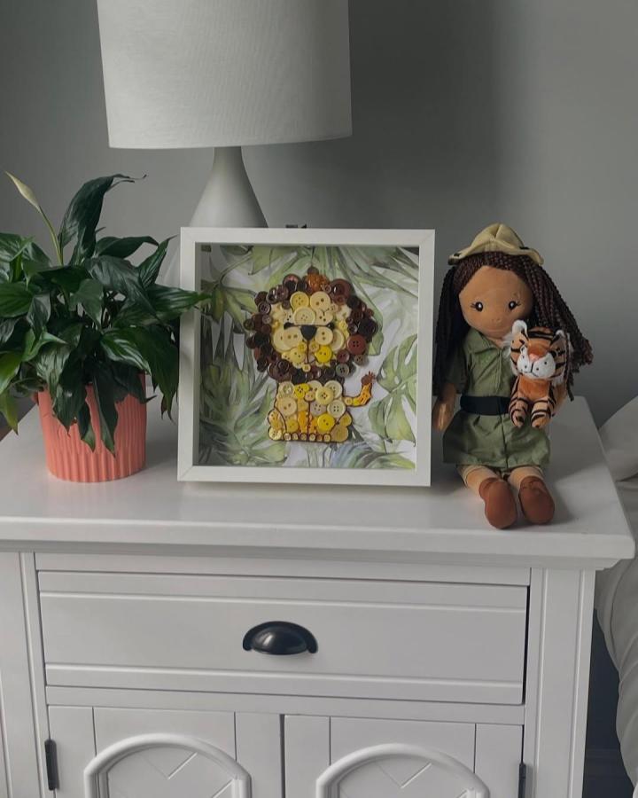Brown and yellow button lion craft in white shadowbox by @riasrocksanduniquegifts with jungle leaf background button crafts for adults playful design.