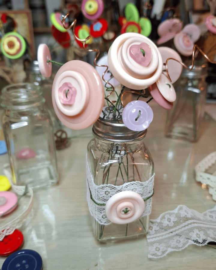 Pastel button flower bouquet in a lace-wrapped glass jar from @carolyn.boulton. Soft pink and lilac button crafts for adults with copper wire stems.