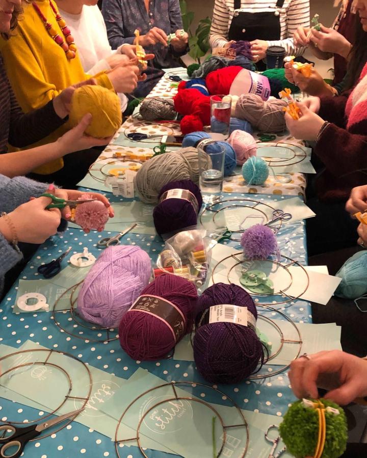 Brightly colored yarns and pom poms on tables with wreath frames from Pom Stitch Tassel at craft night themes for adults gathering.
