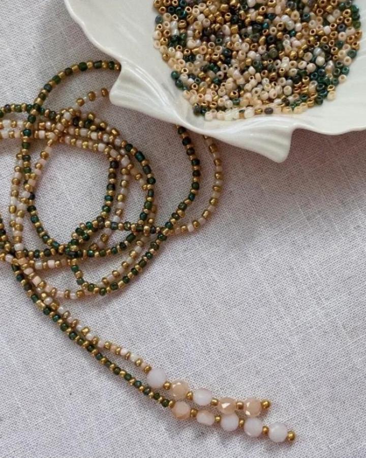 Soft pink, green, and gold beaded necklace on linen fabric from Laura Jade Prado. Elegant craft night themes for adults jewelry idea.