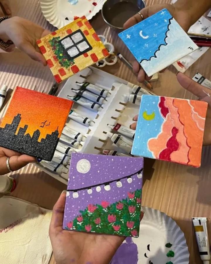 Colorful miniature acrylic paintings held over paint tubes and palettes from @haticedenfikirler showing vibrant small art perfect for craft night themes for adults.