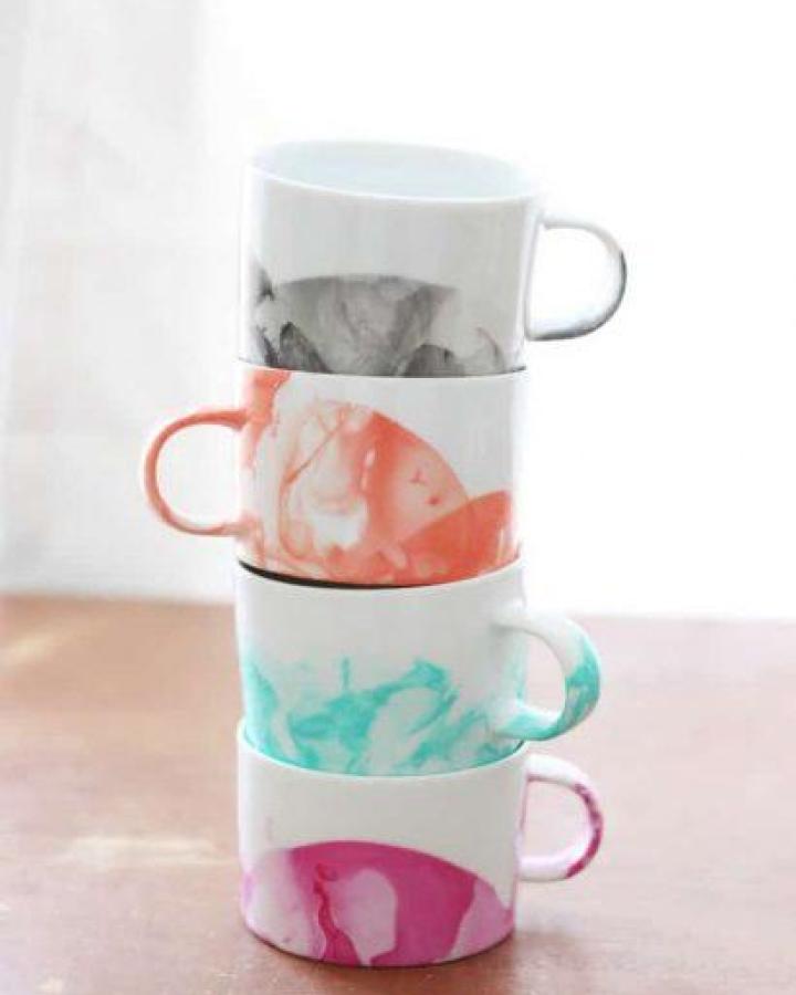 White ceramic mugs with colorful marbled nail polish designs stacked on wood from Mod Podge Rocks. Craft night themes for adults inspiration.