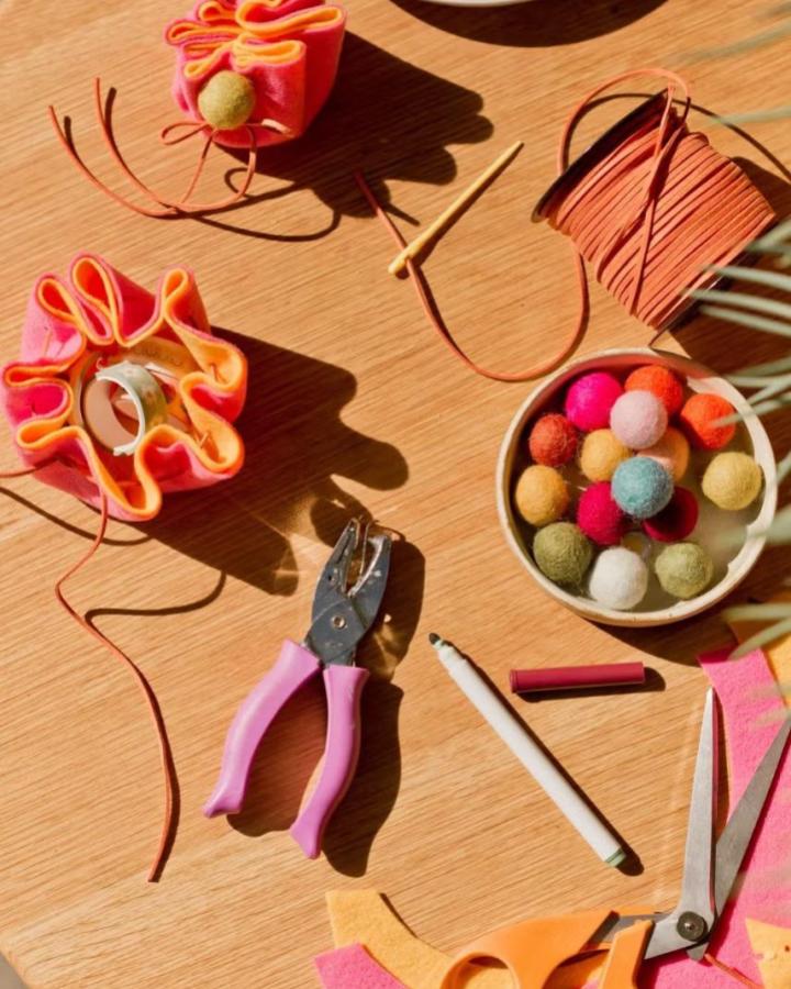 Bright pink and orange felt drawstring pouches with colorful felt balls and crafting tools from Good Housekeeping craft night themes for adults setup