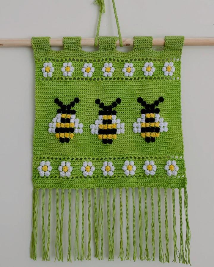 Green crochet wall hanging with bees and daisies from @paulina.s.maraboli featuring playful patterns and fringe detailing.
