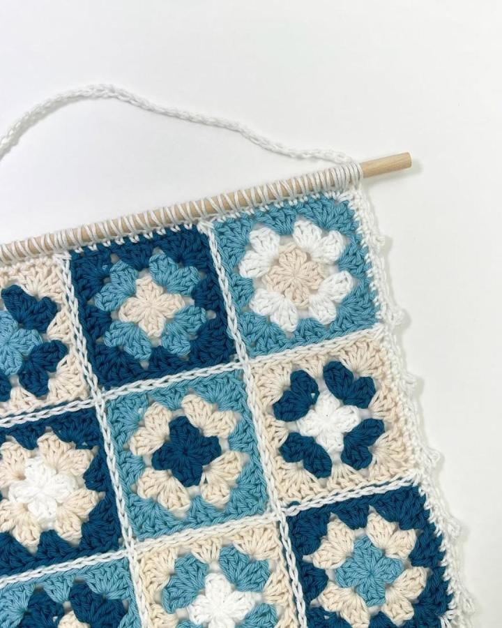 Blue cream and navy granny square crochet wall hanging from @ashtenstitches with a wooden rod and neat white joining for crochet wall hanging ideas