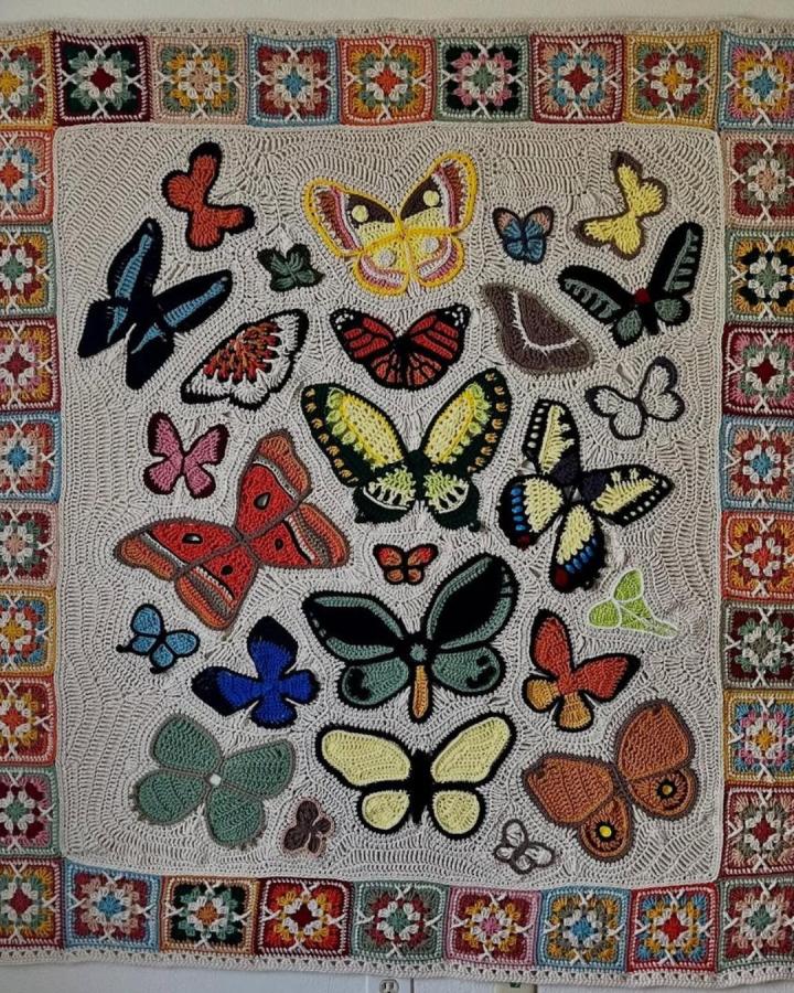 Colorful butterfly crochet wall hanging with granny square border from @kid.crochet. Vibrant yarn and textured neutral background enhance crochet wall hanging ideas.