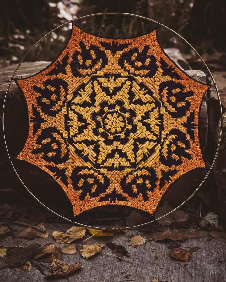 Orange and black crochet wall hanging on metal hoop with jack-o'-lantern faces from @crochet.with.may Halloween themed crochet wall hanging ideas.