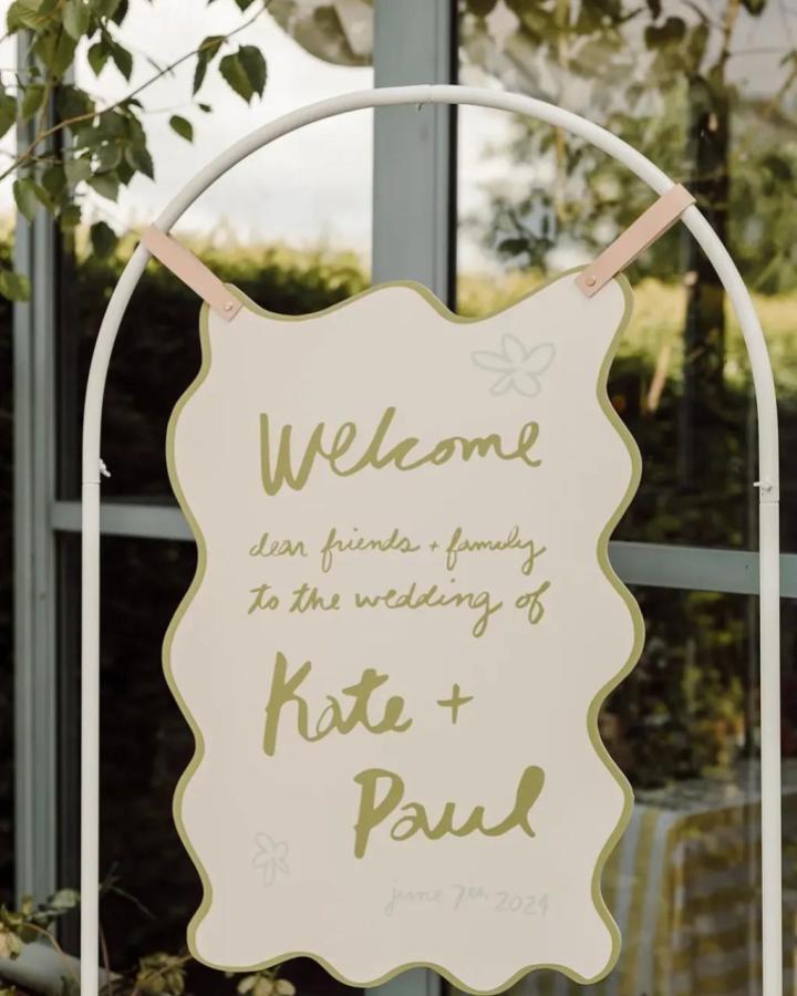 Wavy edged cream wood sign with olive script and leather straps from One Fab Day diy wedding welcome sign ideas simple rustic charm