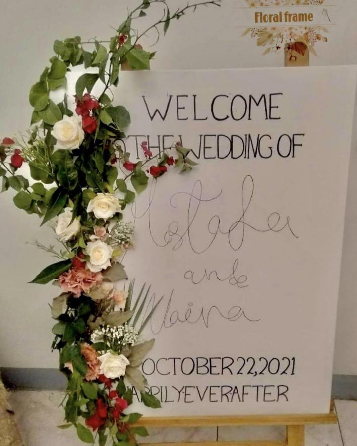 White and red floral accented wedding welcome sign on wooden easel from Amal welcome signs with handwritten lettering and greenery decoration.