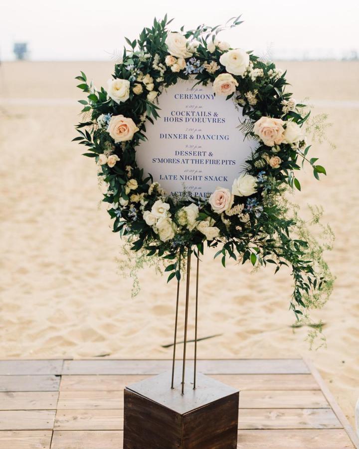 White and blush rose floral wreath on gold rods with wooden base diy wedding welcome sign ideas from Style Me Pretty. Beach ceremony backdrop.