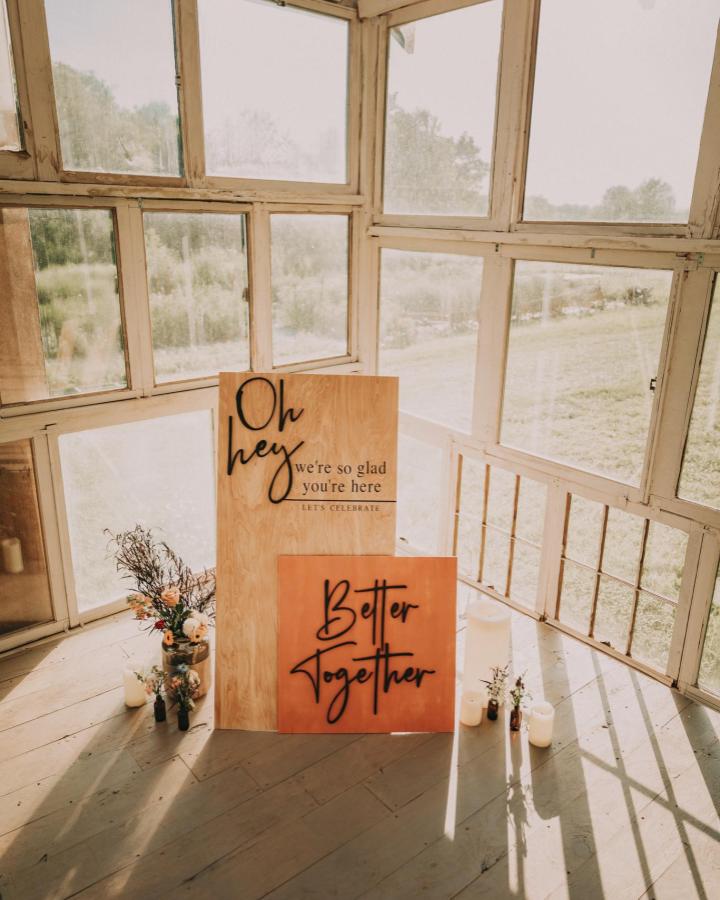 Natural wood wedding welcome signs with black hand-painted lettering and floral accents from Nashville Bride Guide set in sunlit rustic space for diy wedding welcome sign ideas.