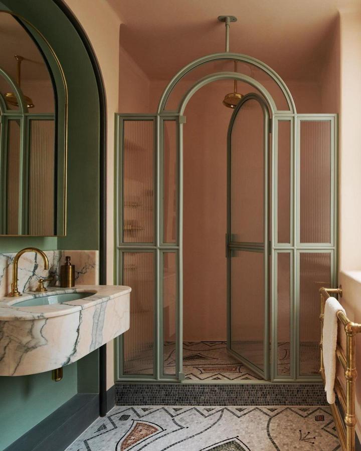 Soft sage green arched shower doors and brass fixtures in a chic bathroom from @ebolognino illustrate green bathroom decor ideas. Elegant and textured design.