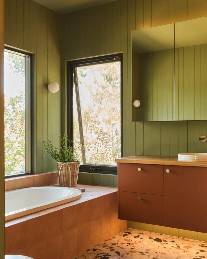 Olive green paneled bathroom walls with terracotta tiles and terrazzo floor from @peninsulaecoconstructions in green bathroom decor ideas. Natural, earthy style.