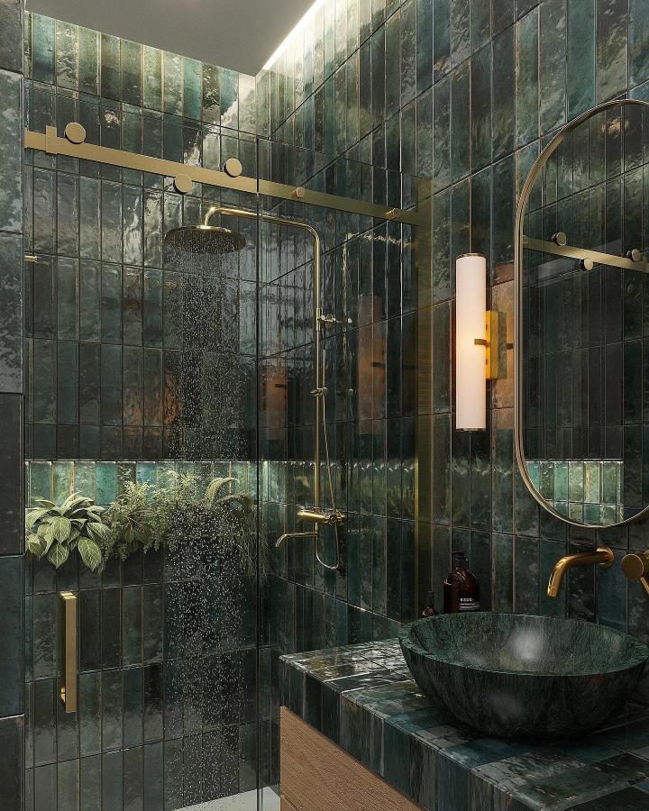 Glossy dark green ceramic tile bathroom with brass fixtures and plants from @designminimal.nl. Moody and inviting green bathroom decor ideas.