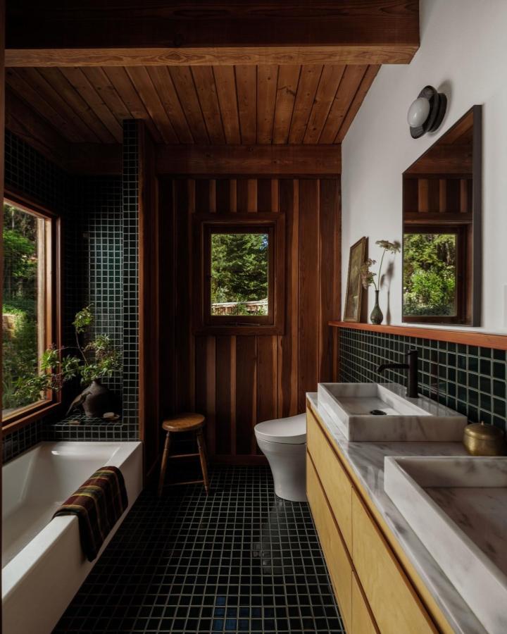 Dark green square tile bathroom with wood paneling and marble sinks from @fireclaytile. Cozy natural green bathroom decor ideas.