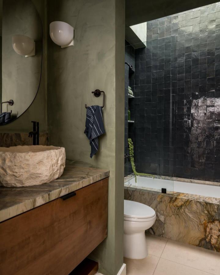 Earthy stone sink and wooden vanity in green bathroom decor ideas from @sagradastudio with textured olive walls and black tile shower surround