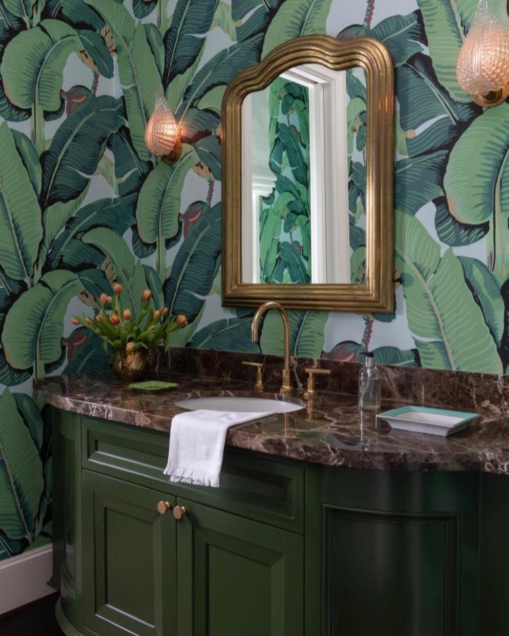 Green tropical leaf wallpaper and dark green vanity with brass fixtures from @ashleygoforth. Bold green bathroom decor ideas with natural and vintage elements.