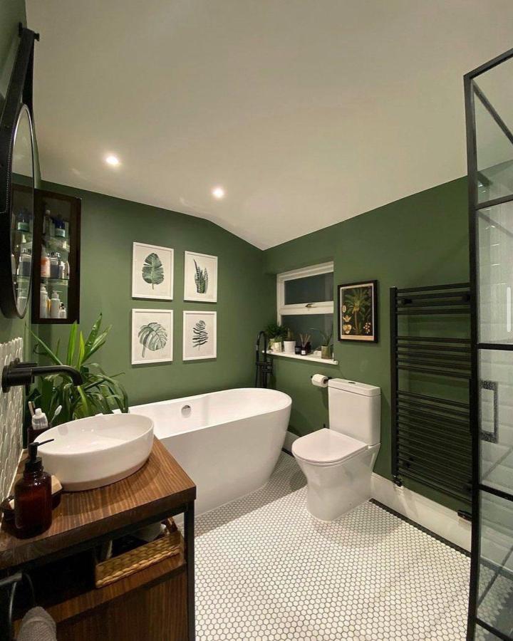 Green matte walls and leafy botanical prints in a bathroom from @renovateno28 with white fixtures and hex tile floor creating cozy green bathroom decor ideas.